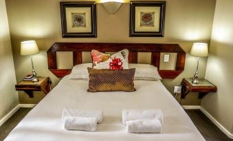 a neatly made bed with white sheets and a wooden headboard , adorned with two folded towels on the foot of the bed at Oxford Lodge Vryheid