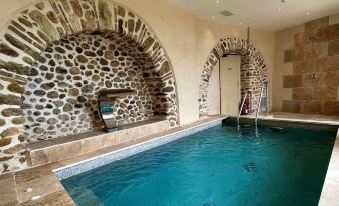 an indoor swimming pool surrounded by stone walls , with a sauna and hot tub visible in the background at Chateau le Cagnard