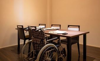 a wheelchair is parked in a room with a dining table and chairs , and a lamp on the table at Kamisuwa Onsen Shinyu
