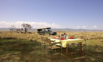 a table with chairs is set up in a field with a jeep driving by in the background at Elewana Lewa Safari Camp
