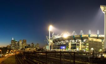 a large stadium at night , with the lights illuminating the building and city skyline in the background at Punthill Ivanhoe