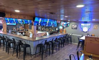 a modern bar with wooden ceiling , large screens on the wall , and black chairs arranged around a long counter at Smoky Falls Lodge