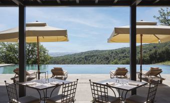 an outdoor dining area with tables and chairs overlooking a body of water , creating a serene atmosphere at Rosewood Castiglion del Bosco