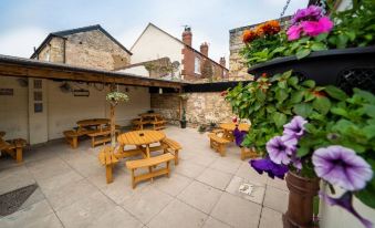 a wooden patio area with tables and chairs , surrounded by flowers and a stone building at The Oddfellows Arms
