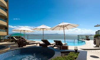 a pool with lounge chairs and umbrellas is overlooking the ocean and a body of water at Majestic Palace Hotel