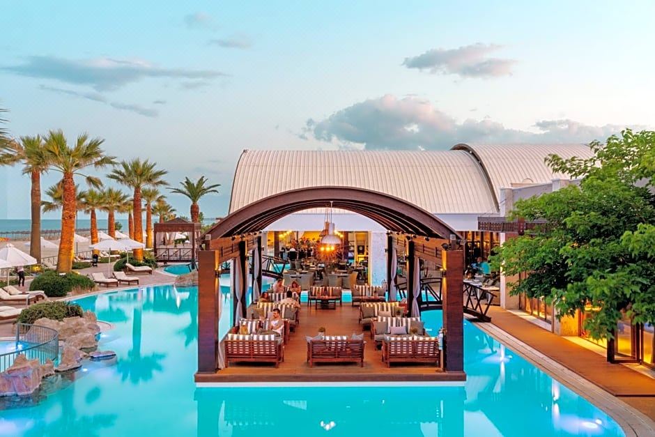a large outdoor pool surrounded by lounge chairs and umbrellas , with palm trees in the background at Mediterranean Village Hotel & Spa