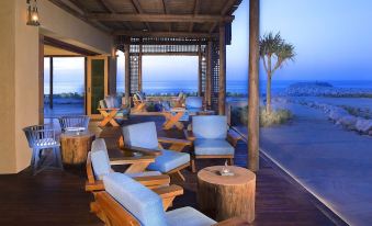 a wooden deck with multiple chairs and tables set up for outdoor dining , overlooking the ocean at Anantara Desert Islands Resort & Spa