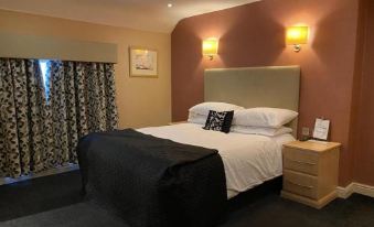 a large bed with a black headboard and white linens is in a room with two wall sconces at The Windmill Inn