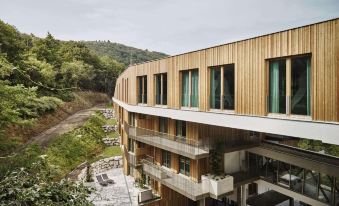 a modern wooden building with large windows and a balcony , surrounded by lush greenery and mountains at Steigenberger Hotel and Spa, Krems