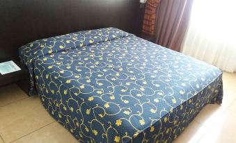 a neatly made bed with blue and yellow floral sheets , positioned next to a window with curtains at Hotel Panorama