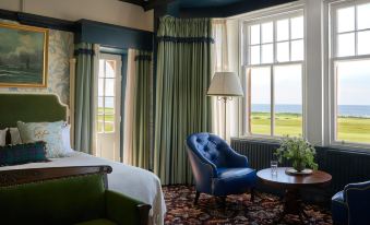 a luxurious bedroom with a large window overlooking the ocean , a comfortable bed , and a green armchair at Marine Troon