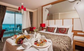 a luxurious hotel room with a king - sized bed , a dining table with food , and a view of the ocean at Q Premium Resort Hotel
