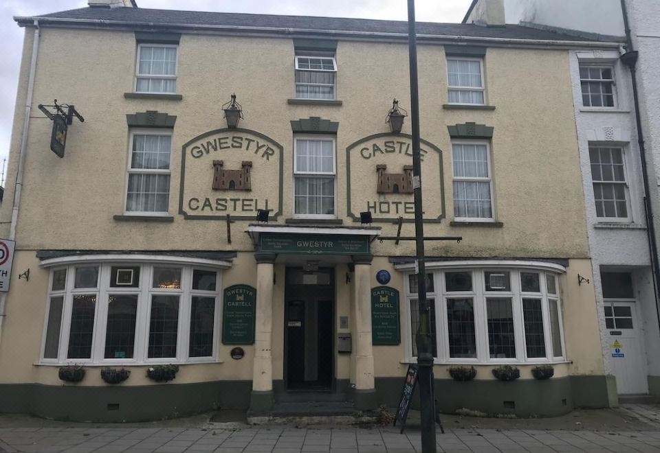 "a traditional english pub with a sign for "" omertity castel hotel "" and two green banners above the entrance" at The Castle Hotel