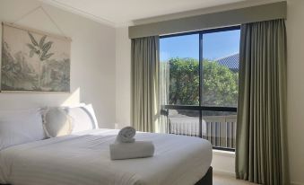 a well - arranged hotel room with white walls , large windows offering views of trees and mountains , and a comfortable bed with rolled towels at Eastcoaster Tasmania