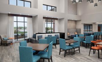 a modern , open - concept dining area with multiple tables and chairs arranged around a large window at Hampton Inn & Suites Bridgeview Chicago