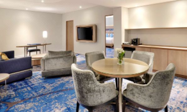 a modern living room with a blue carpeted floor , gray armchairs , and a wooden coffee table at Novotel Jakarta Mangga Dua Square