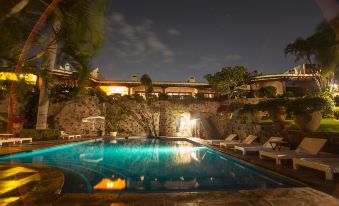 a large outdoor swimming pool surrounded by a stone wall , with several lounge chairs and umbrellas placed around the pool area at Las Mañanitas