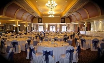 a large , elegant banquet hall with multiple round tables covered in white tablecloths and adorned with blue chairs at Mulroy Woods Hotel