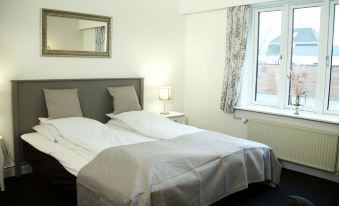 a clean and well - organized bedroom with a white bed , black floor , and a window with curtains at Dronninglund Hotel