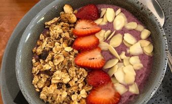 a bowl filled with a delicious purple smoothie topped with granola , strawberries , and almonds , sitting on a dining table at Motel Goolwa