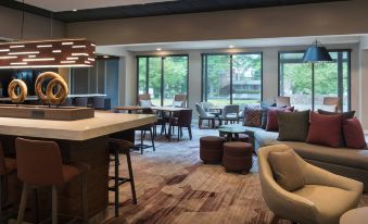 a modern hotel lobby with comfortable seating , a bar area , and large windows offering views of trees outside at Courtyard Lincroft Red Bank
