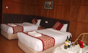 a hotel room with two beds , each bed having white sheets and red pillows , along with a bottle of wine on the nightstand at Hotel Srinagar