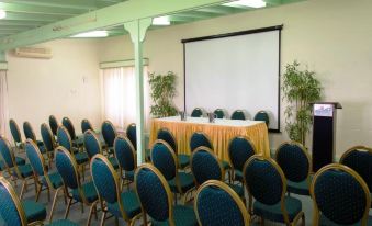 a conference room with green chairs arranged in rows , a projector screen on the wall , and a whiteboard at Bougainvillea Barbados