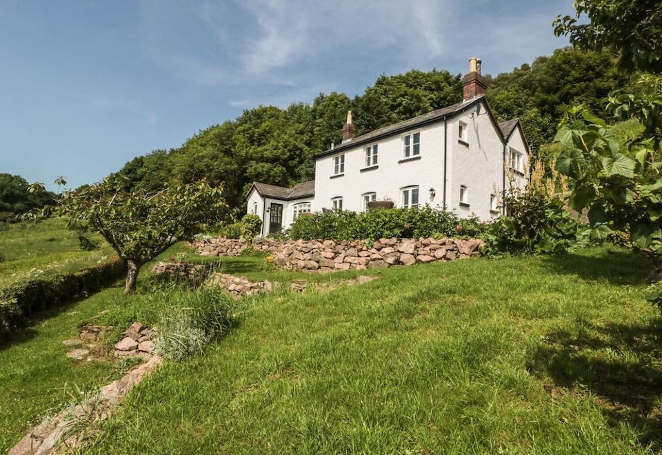 a large white house surrounded by green grass and trees , located on a hillside overlooking a body of water at Lilac Cottage