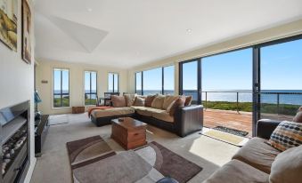 a spacious living room with a large couch , coffee table , and floor - to - ceiling windows overlooking the ocean at Seaspray