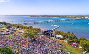 a large crowd of people gathered on a grassy field , with a bridge in the background at BIG4 Sandstone Point Holiday Resort