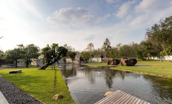 a serene park with a wooden bridge over a pond , surrounded by lush greenery and trees at Berugo Cottage