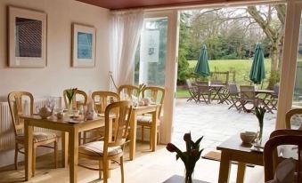 a dining room with wooden chairs and tables , surrounded by windows that offer a view of the outdoors at Brasteds