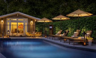 a beautiful swimming pool and outdoor area with umbrellas , lounge chairs , and a house in the background at The Cottages Hotel