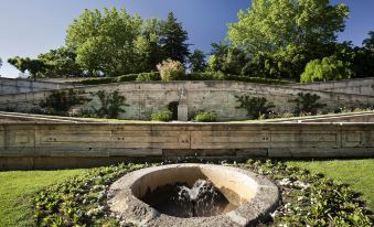 a garden with a large circular pond surrounded by trees and bushes , creating a picturesque scene at Novotel Avignon Nord