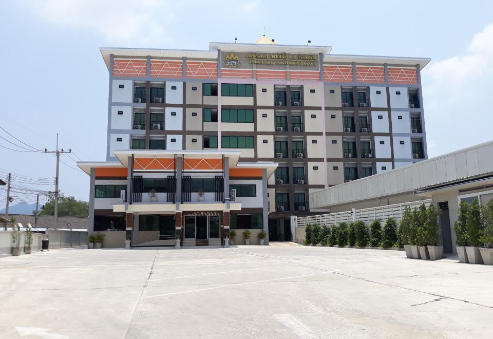 a large building with orange and white accents is surrounded by a parking lot and trees at Phetlada Pavilion & Resort