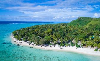 a lush green hillside with trees and buildings , situated on a beach near the ocean at Small Luxury Hotels of the World - Pacific Resort Aitutaki