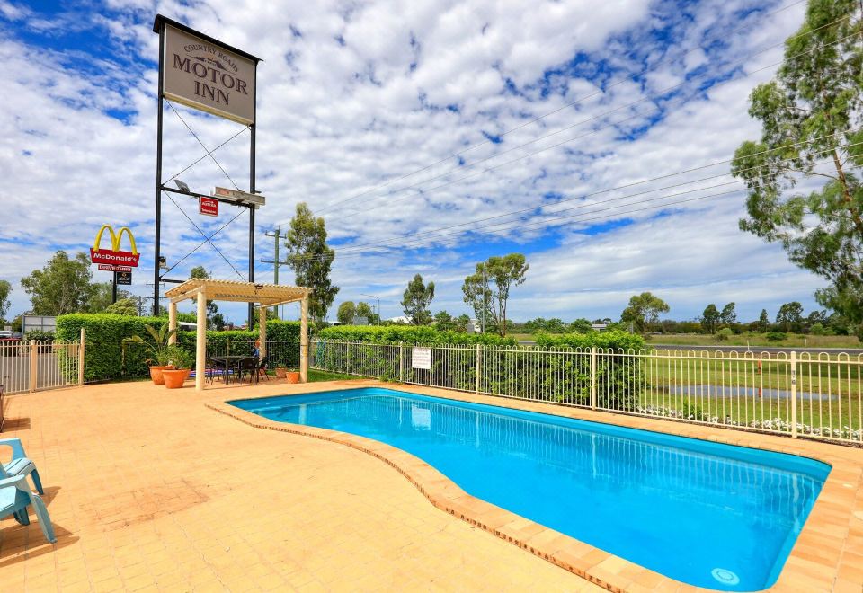 "a pool with a sign that says "" moreton bay inn "" and a basketball hoop nearby" at Country Roads Motor Inn