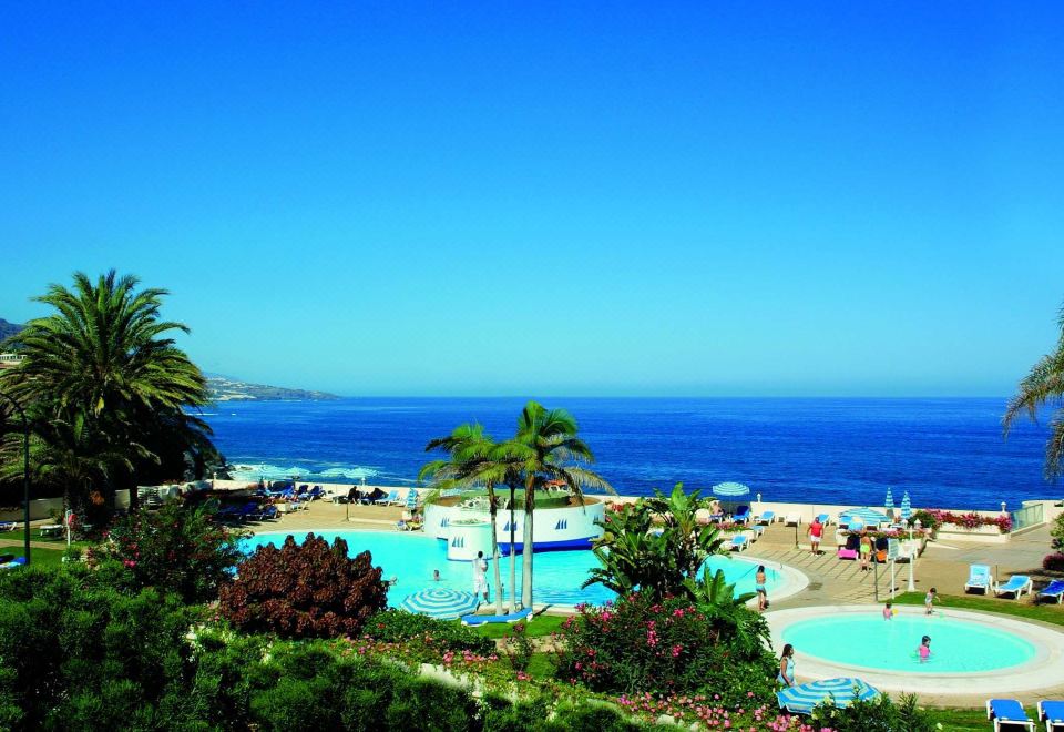 a resort with a large pool surrounded by palm trees and the ocean in the background at Precise Resort Tenerife