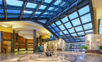 a large , modern hotel lobby with a glass ceiling and a marble floor , as well as several chairs and tables in the area at Lykia World Antalya