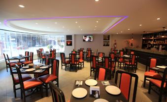 a restaurant with red and black chairs and tables , a tv on the wall , and windows at Hotel Astor