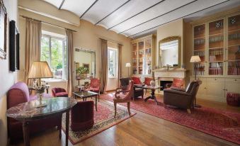 a spacious living room with wooden floors , multiple chairs , and a fireplace , decorated with red curtains and a rug on the floor at Hotel Vannucci