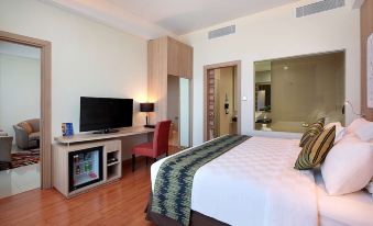 a modern hotel room with a bed , television , and desk , all set against white walls and wooden floors at Galaxy Hotel Banjarmasin