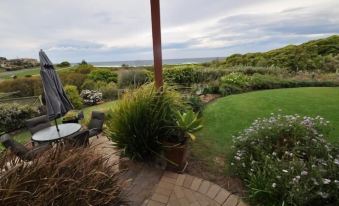 a beautiful garden with lush greenery , a view of the ocean , and a patio area surrounded by plants at Beachfront Apartments