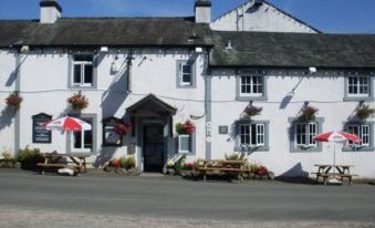 a white building with a red awning , umbrellas , and potted plants is situated in front of a street at The Bridge Inn