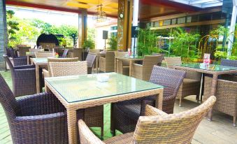 a glass dining table surrounded by wicker chairs in an outdoor setting , with a view of greenery outside at Sapphire Sky Hotel & Conference