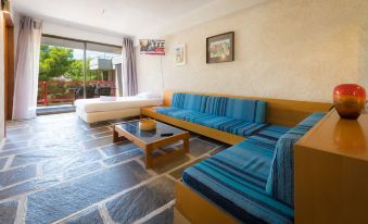 a cozy living room with blue couches , a coffee table , and a tv . also a bed in the room at Apollonia Hotel Apartments