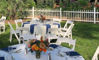 a well - decorated outdoor dining area with white tables and blue napkins , surrounded by a white fence at Dowds Country Inn