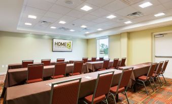 a conference room with red chairs and tables , a large screen on the wall , and a window at Home2 Suites by Hilton Omaha/West