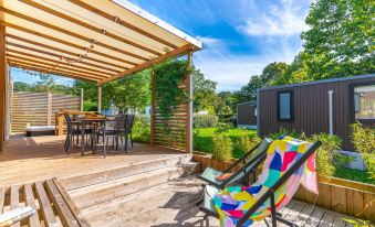 a wooden deck with a dining table , chairs , and a barbecue grill , surrounded by greenery at Camping le Parc de Paris