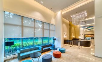 a modern living room with a large window , blue couches , and various seating options for guests at Holiday Inn Express Kolkata Airport